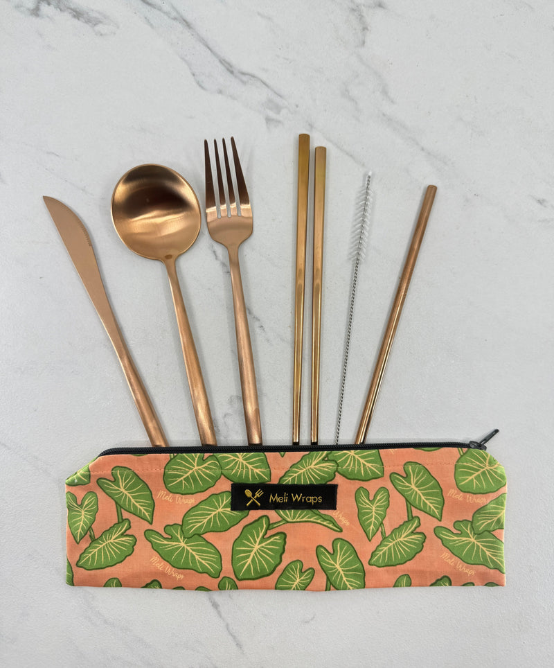 Set of gold cutlery and straws in a leaf-patterned pouch on a marble background