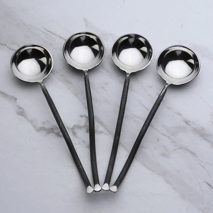 Four black-handled spoons with silver bowls on a marble surface