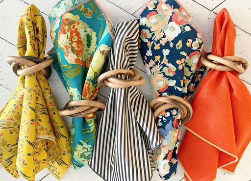 Set of colorful napkins tied with wooden rings on a light wooden surface