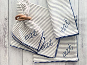 Striped towels with 'eat' embroidery on a wooden surface