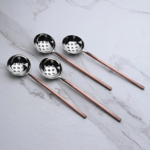 Set of four ladle spoons with copper handles on a marble surface