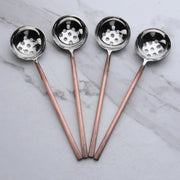 Four metal ladles slotted spoons with copper handles on a marble surface
