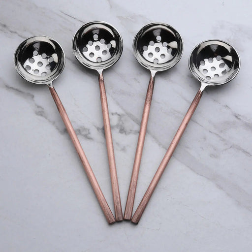 Four metal ladles slotted spoons with copper handles on a marble surface