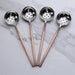 Four metal ladles slotted spoons with copper handles on a marble surface