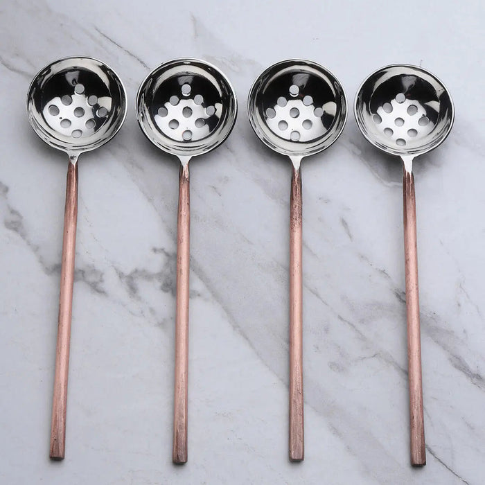 Four ladles slotted spoons with copper handles on a marble background