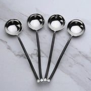 Four black-handled spoons with silver bowls on a marble surface