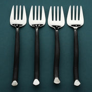 Four silver forks with black handles on a teal background