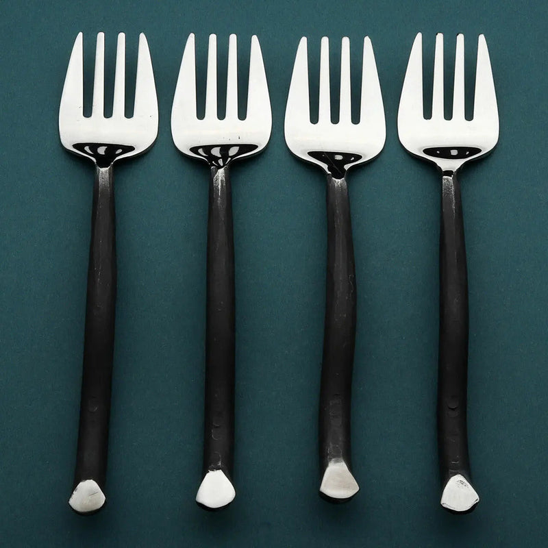 Four silver forks with black handles on a teal background