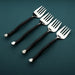 Four black-handled forks on a dark green background